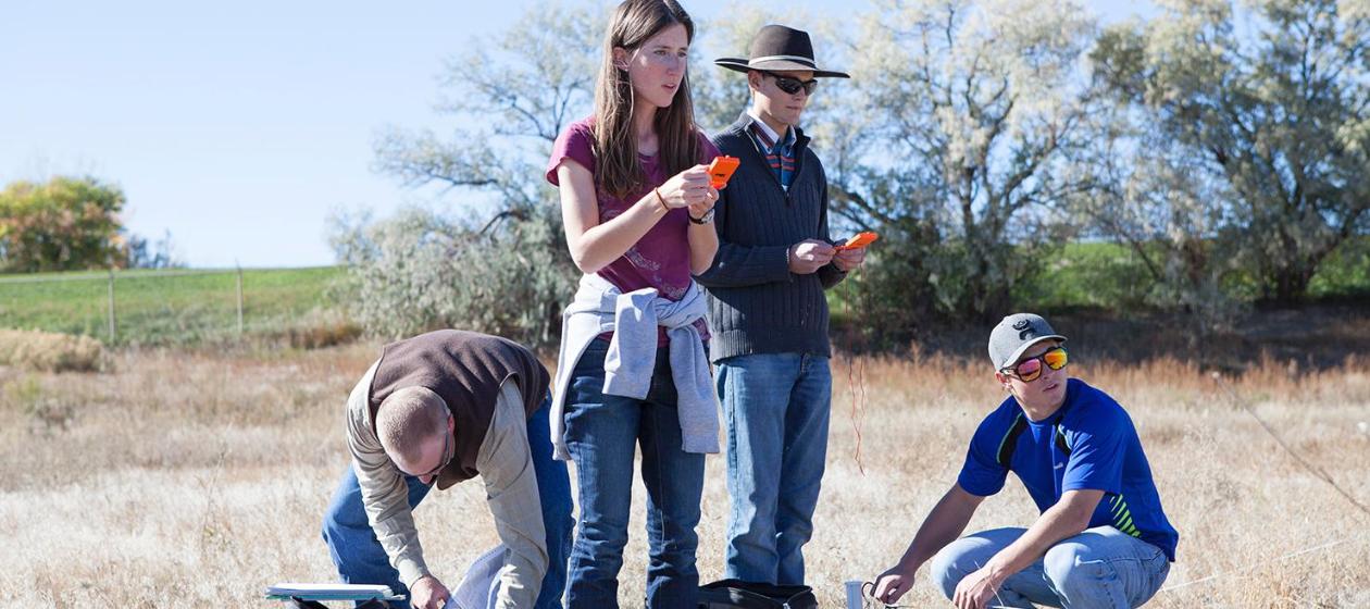 Four students outdoor in the sun surveying a field