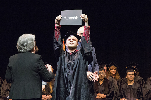 HEQ graduate holds his diploma above his head