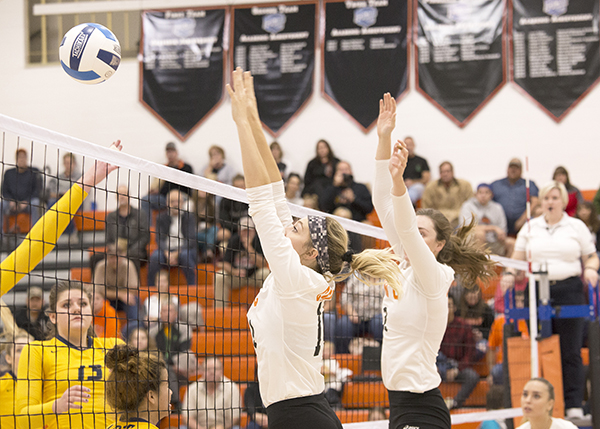 Two CWC volleyball players block the ball at the net