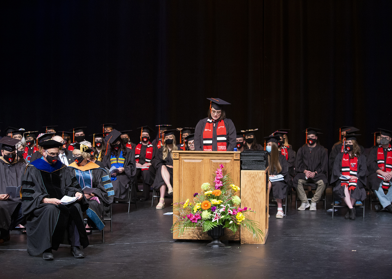 graduate speaker stands at the podium with graduates on stage