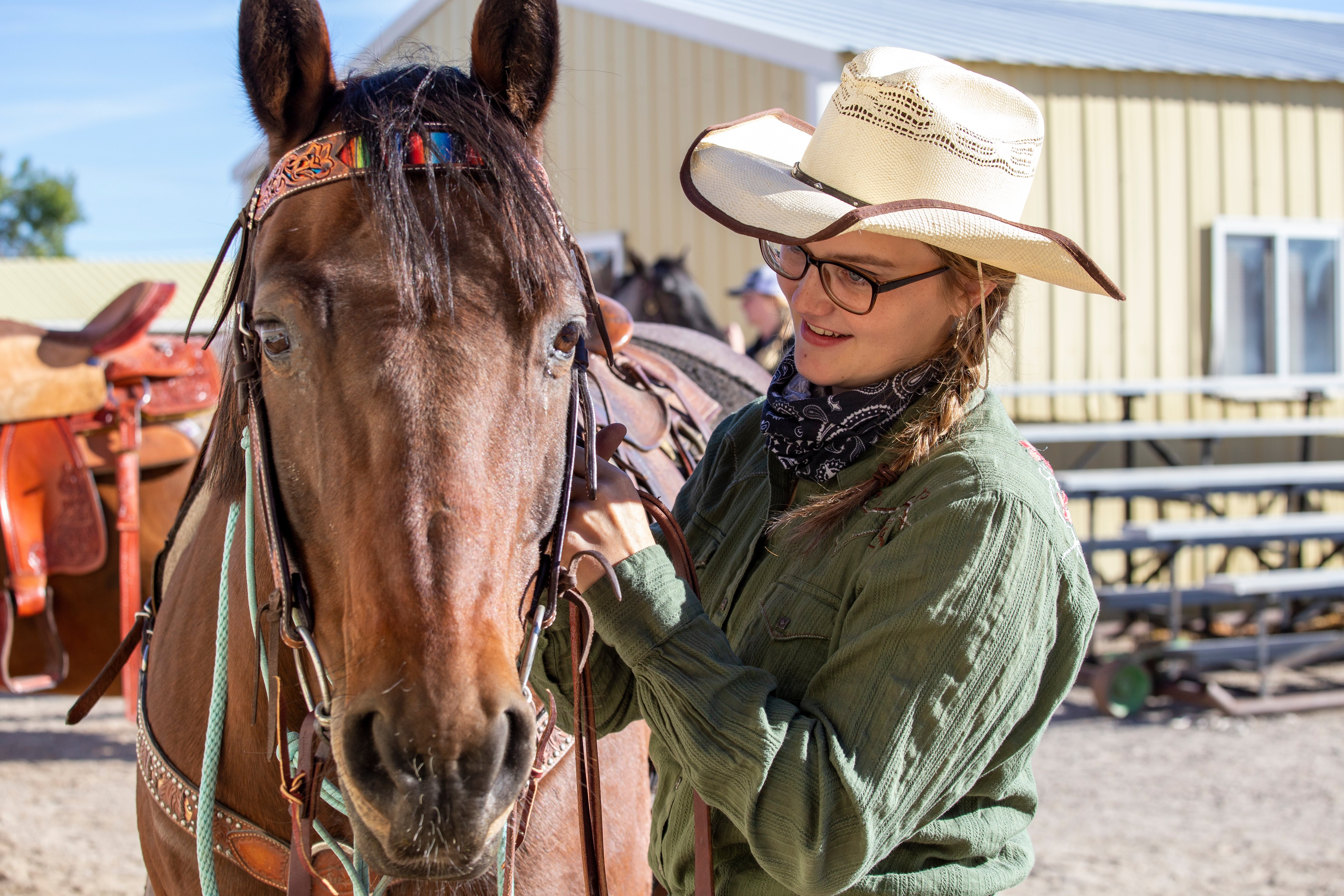 Girl in cowboy hat and green shirt with brown hair petting a brown horse