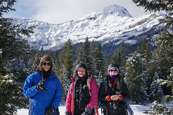 Three students posing in the winter with a snowy mountain in the background