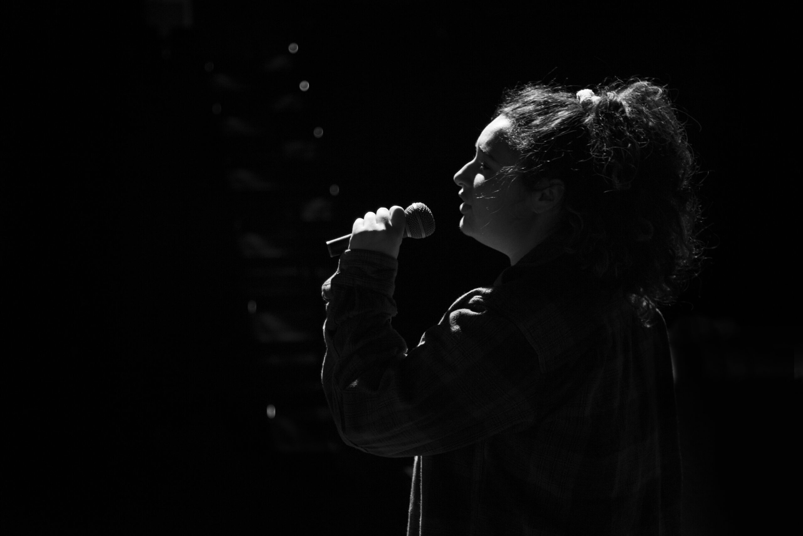 photo of CWC student Tapaynga Hill backlit, singing on stage with a microphone