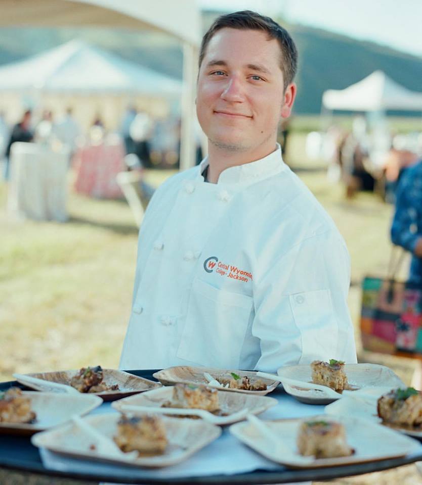 Zack Ward culinary student in smock in front of dessert table