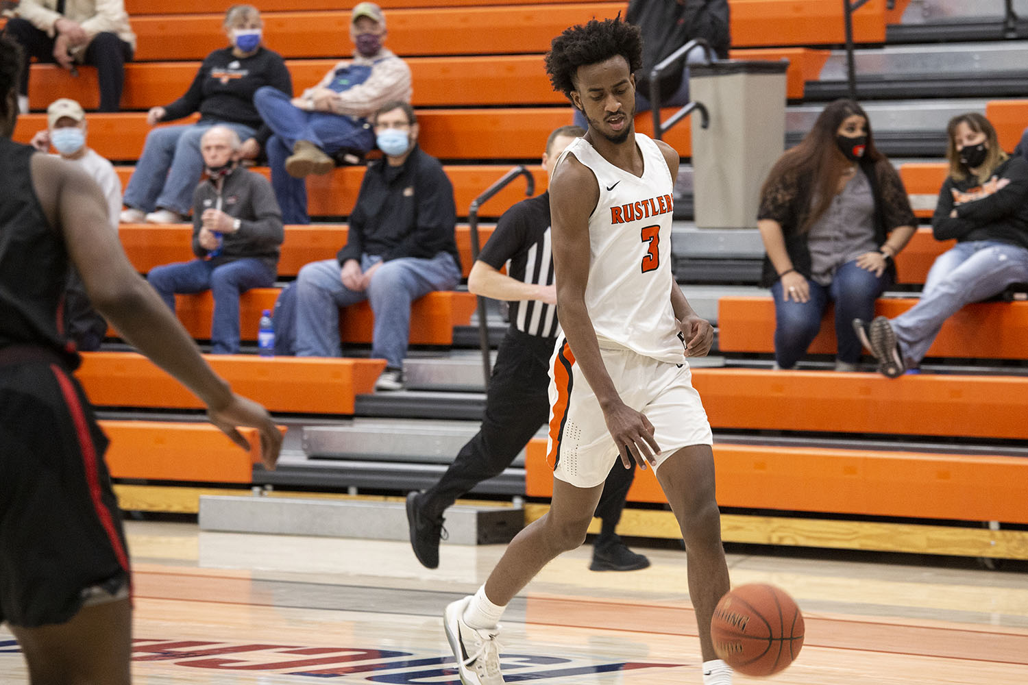 Rustler men's basketball player dribbles the ball away from the opponent.