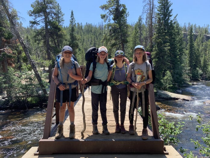 Four middle school aged students with backpacks standing on a bridge in the mountains