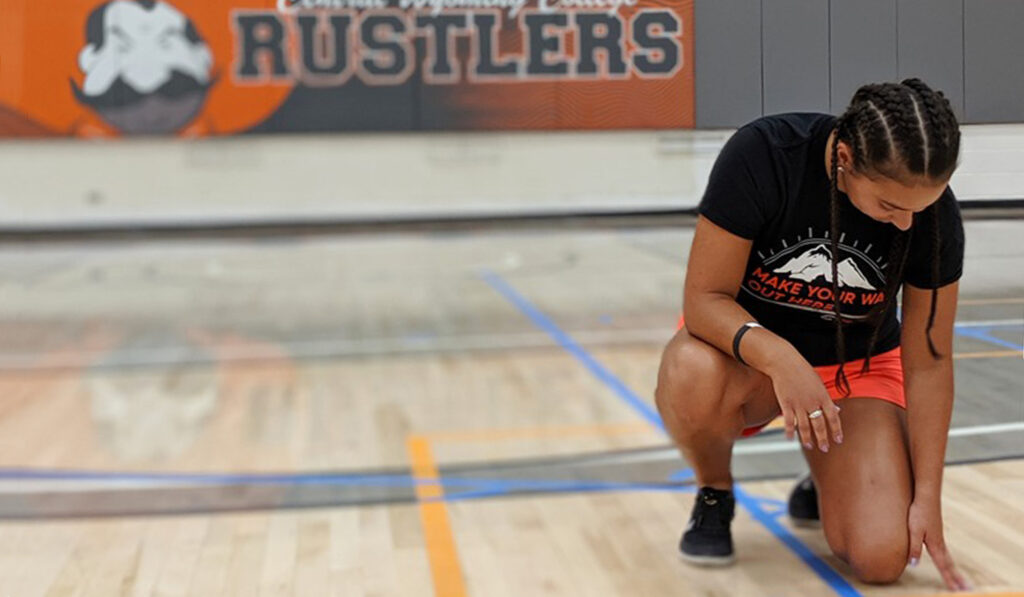 student kneeling on the gym floor with the gym mat of the mascot behind her